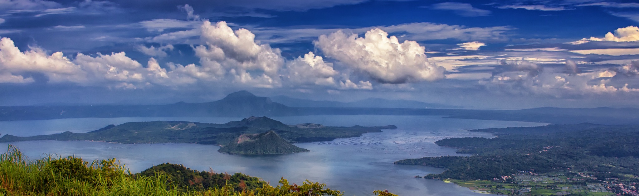 A photograph of a lake with a small island in it, fluffy low clouds hovering above.